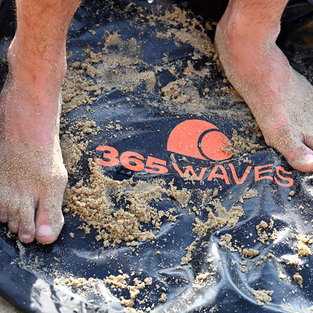 A man with sandy feet standing on the 365Waves Changing Mat / Dry Bag