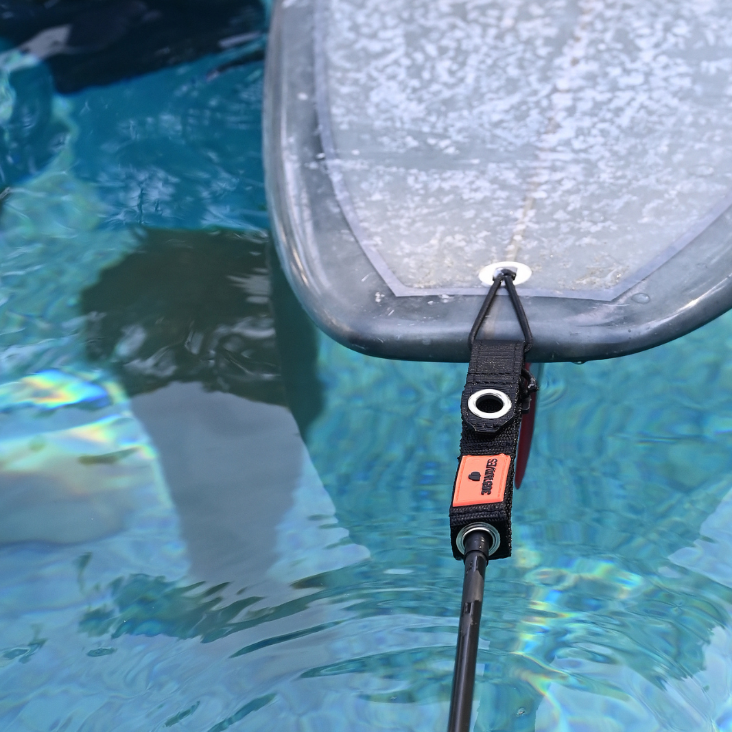 A detail of the 365Waves Surf Resistance Trainer connected to a surfboard in a swimming pool