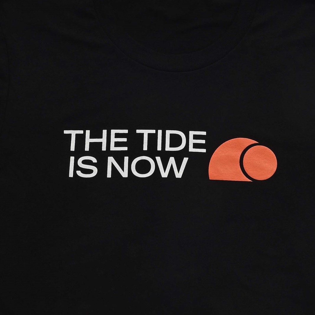 A close up of a black tshirt with The Tide Is Now in white and an orange 365Waves logo