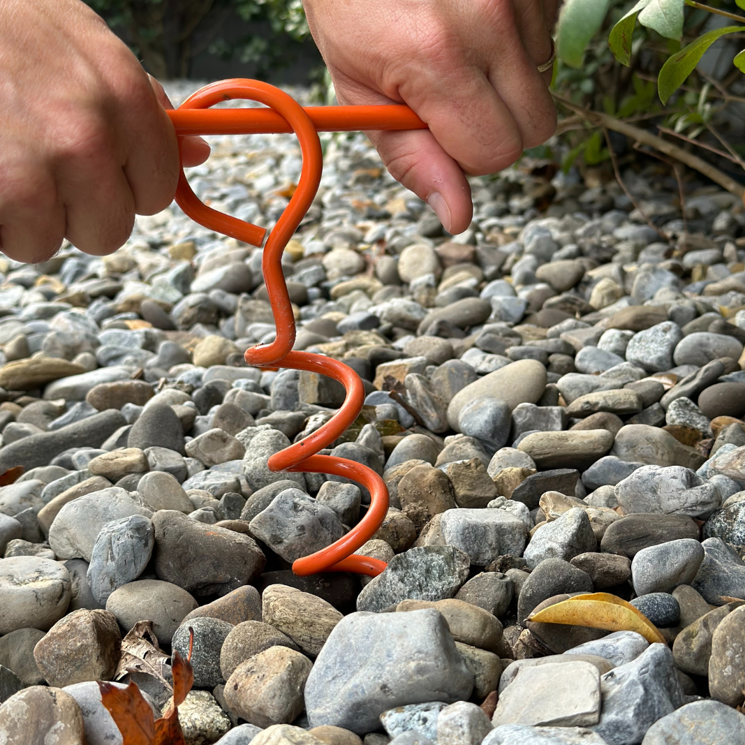 A man twisting the orange anchor of the 365Waves Surf Resistance Training Kit into a gravel ground