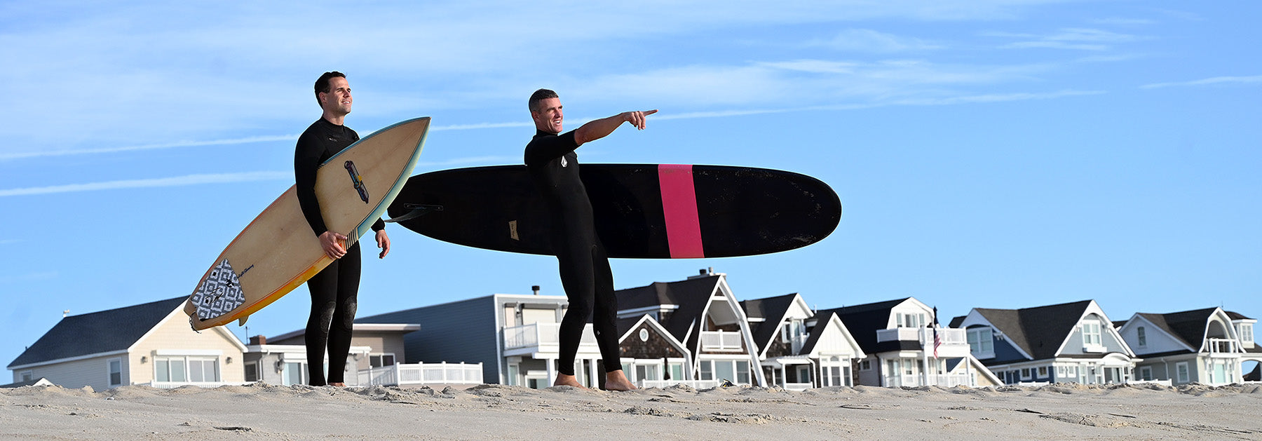 Two men standing on a beach carrying surfboards