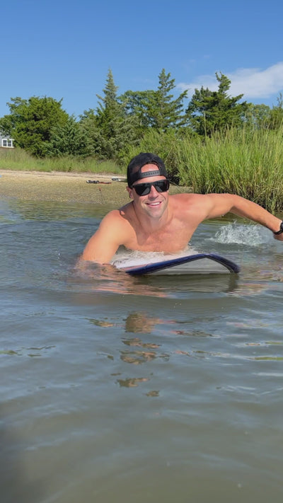 Man paddling on a surfboard in a lake using the 365Waves Resistance Surf Trainer