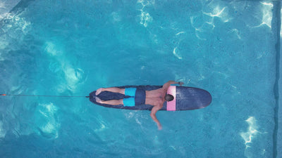 Video of a man paddling on a surfboard in a pool using the resistance surf trainer